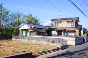 L字型に並ぶ一部2階建ての住宅で、道路沿いに建っており、隣が空き地になっている物件の写真