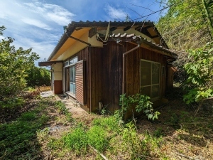 周りに草木が生い茂っており、茶色の外壁で瓦屋根、木像平屋建ての建物の物件の写