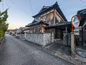 道路に面して塀に囲まれた木造2階建ての住宅の外観写真