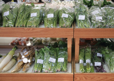 ほうれん草や大根などの新鮮な野菜が木製の棚に並んでいる店内の写真
