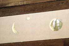 白い長方形の紙に右側に円、中央上部に小さな白い丸、左側に三日月のような形が描かれている写真