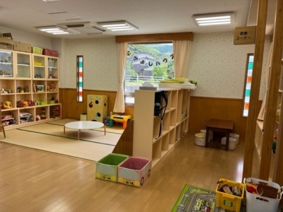 左側は壁におもちゃなどが収納された棚と丸テーブルがある畳のコーナー、右側は机と丸椅子が置かれているコーナーが3段のボックスで仕切られている子育て支援センターの室内を写した写真