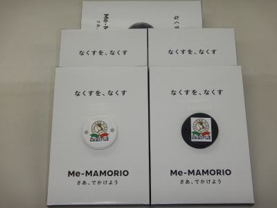 「なくすを、なくす Me-MAMORINO さあ、でかけよう」と記載された白い箱の上に置かれた丸い小型タグの写真