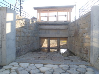 地面に石畳、両側に石が積まれて出来た壁、奥に樋蓋が見える移築復元された土手町南蛮樋を正面から写した写真