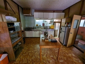 奥に流し台があり、左側に食器棚、中央にテーブル、右側に冷蔵庫が置かれている台所の写真