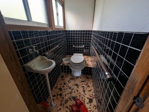 壁の下半分が黒いタイルになっている和式トイレにポータブルトイレをつけたトイレ内を写した写真