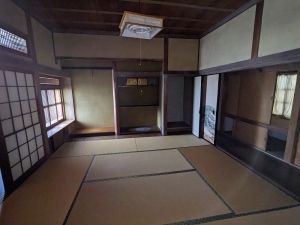 奥に床の間のある和室、和室の隣のふすまが開けられ、廊下がある室内の写真