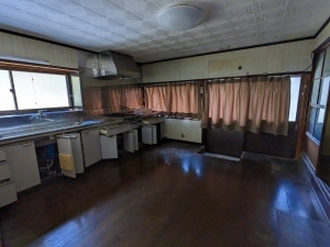 小窓がある左側の壁に流し台が設置され、正面窓にカーテンが掛けられている台所を写した写真