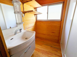 洗面台の横に木製の2段の棚があり、右手に浴室の入り口がある脱衣室の写真