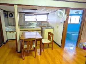 奥にキッチン、ダイニングテーブルがある右側に浴室の入り口が見える台所の写真