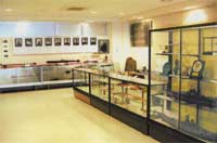 展示品の入ったガラスケースが室内に並び、壁に写真付きのパネルが展示されている展示室内の写真